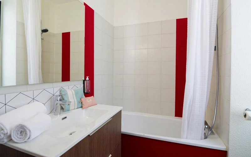 Salle de bain avec baignoire, meuble vasque et touches de rouge dans la Loge de la troupe à l'Hôtel des Artistes